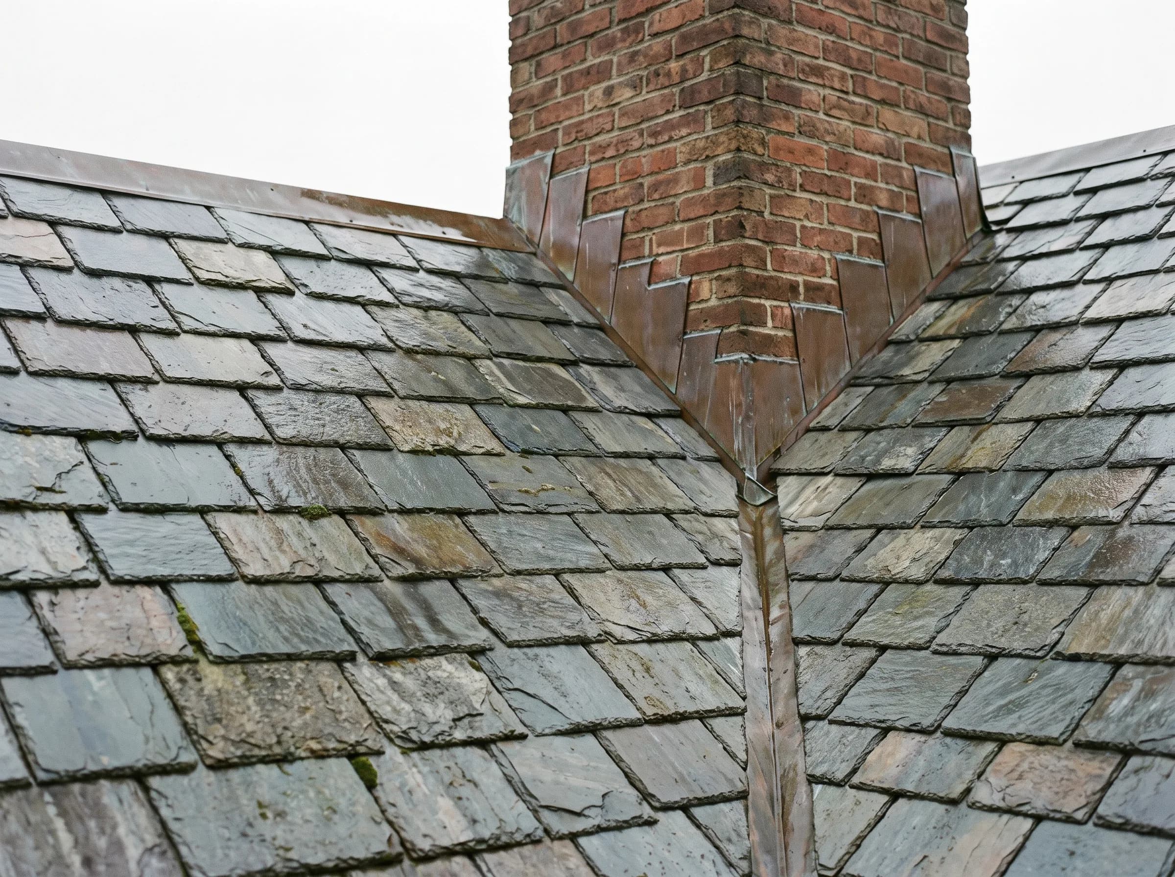 Graduated courses of weathered natural slate tiles on a steep historic roof, illustrative